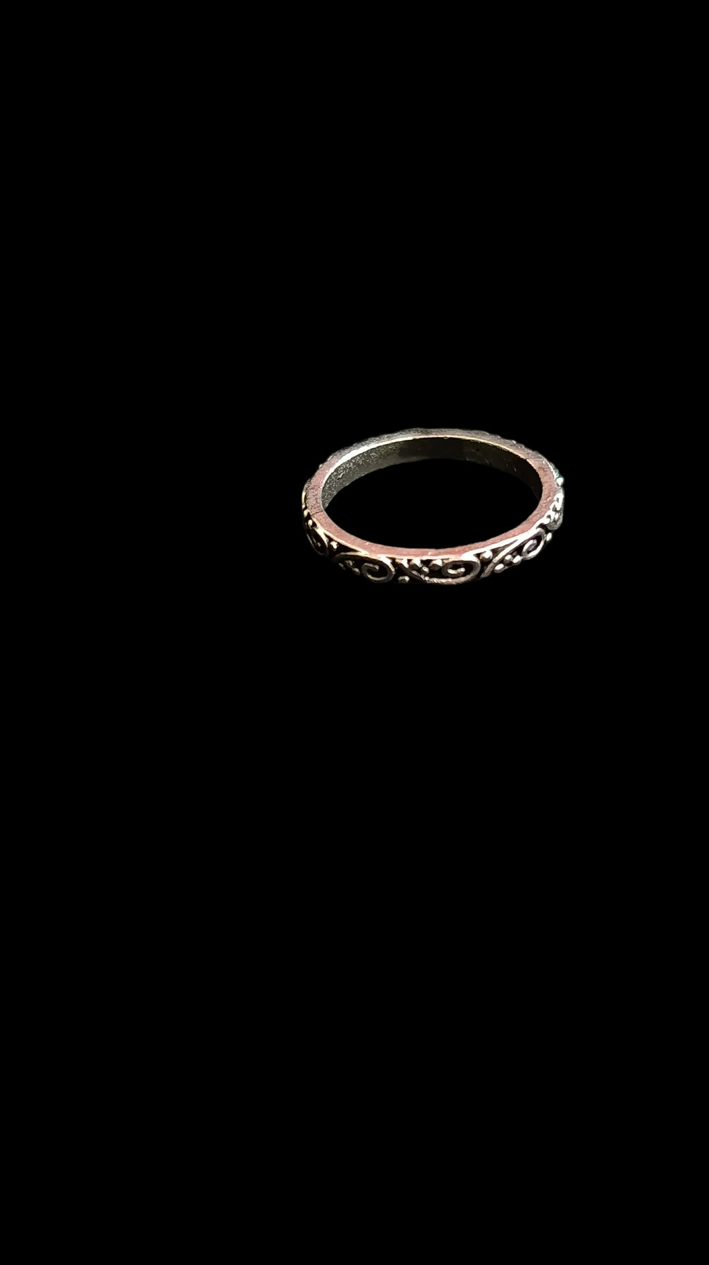Silver ring with intricate design on a black fabric background